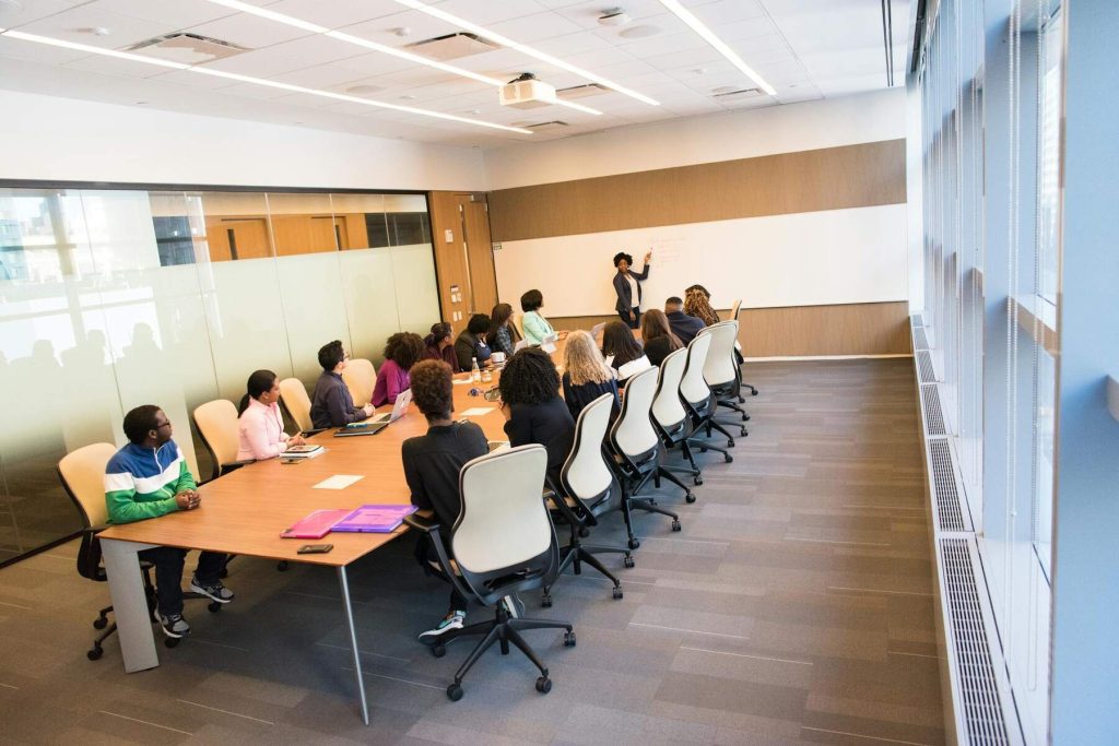 A professional team in a conference room attentively listening to a presenter writing on a whiteboard
