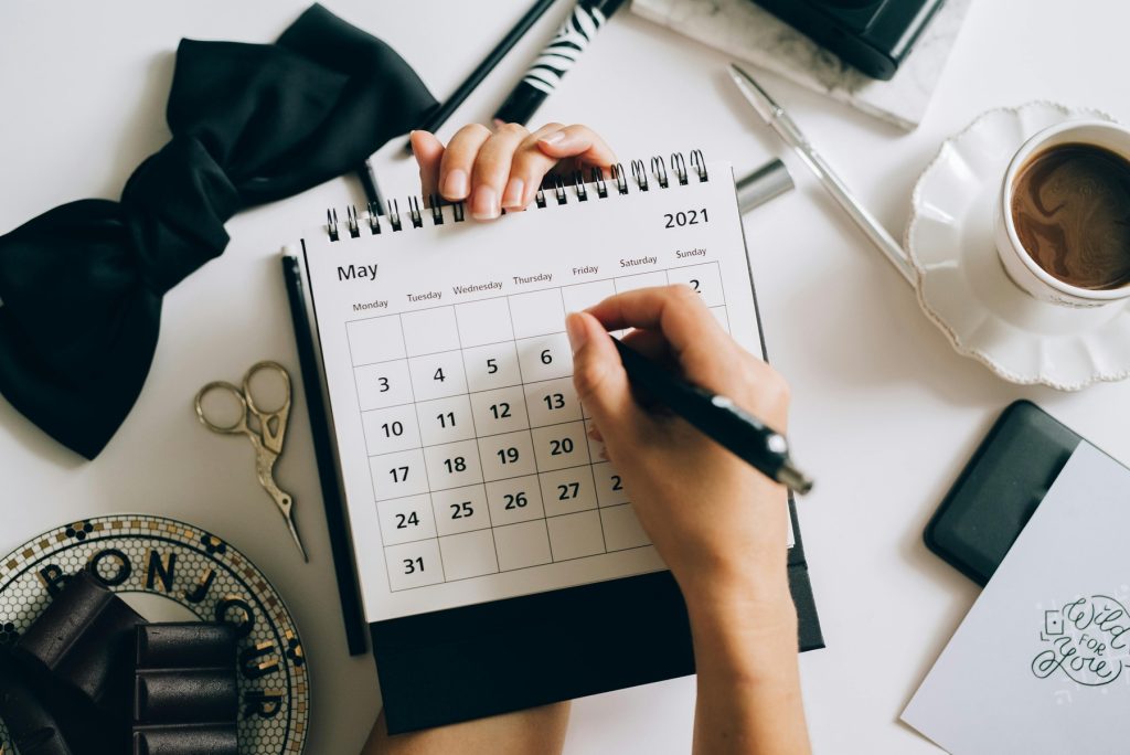 A person writing on a paper calendar for May 2021 with a black pen