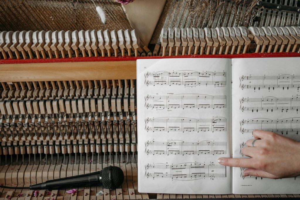 An open piano with exposed hammers and strings, alongside a music sheet and a microphone