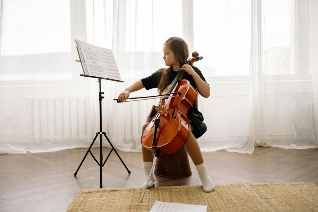 A young girl playing the cello in a bright, elegant room with a music stand in front of her