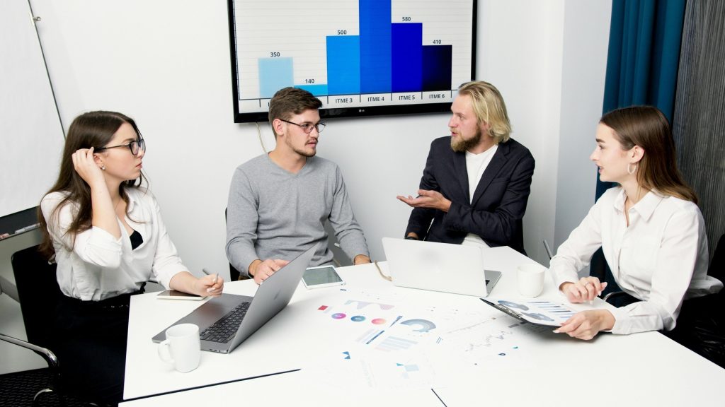 A group of four professionals sitting around a white conference table, engaged in a discussion