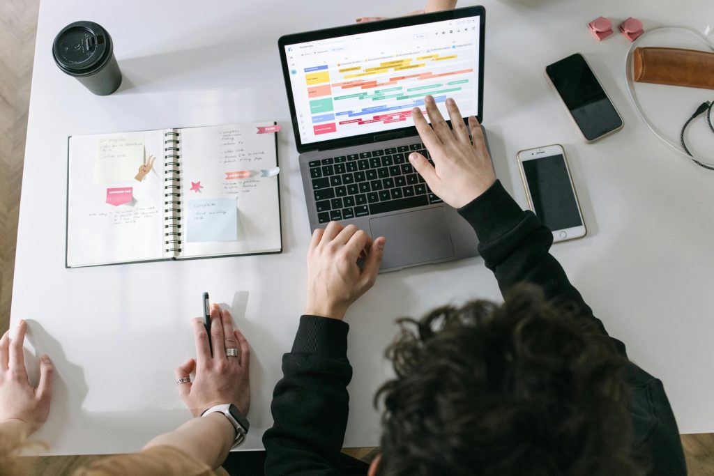 A collaborative work session with a digital calendar on a laptop screen, surrounded by a notebook and smartphones