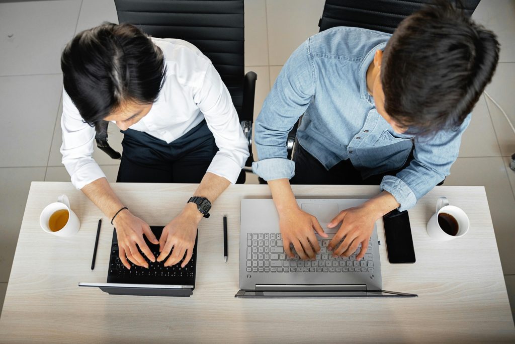 Two professionals working side by side on their laptops, with coffee cups nearby