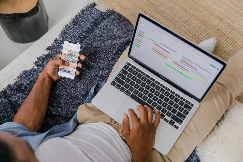 A person managing their schedule using a digital calendar on a laptop while browsing images on a smartphone