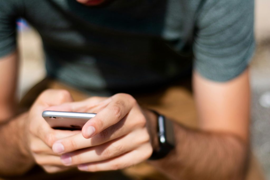 A person wearing a gray t-shirt using a smartphone, focused on the screen.