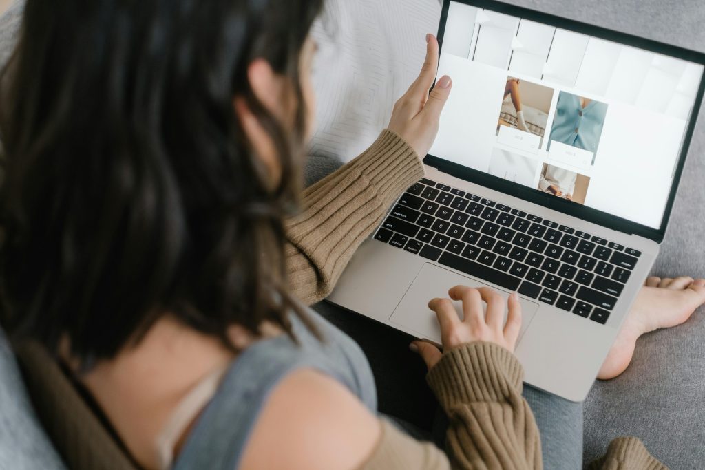 A woman with dark hair sits on a couch, using a laptop to browse an online store.