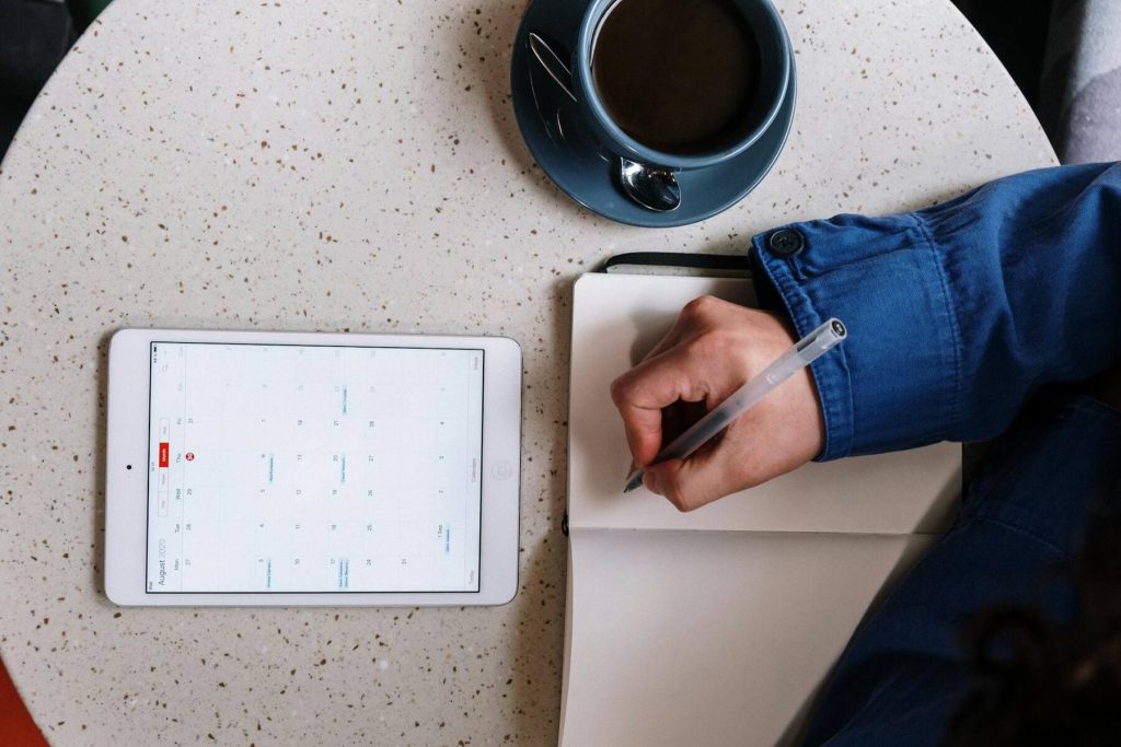 A person writes on a tablet with a pen, while a coffee cup sits nearby on the table
