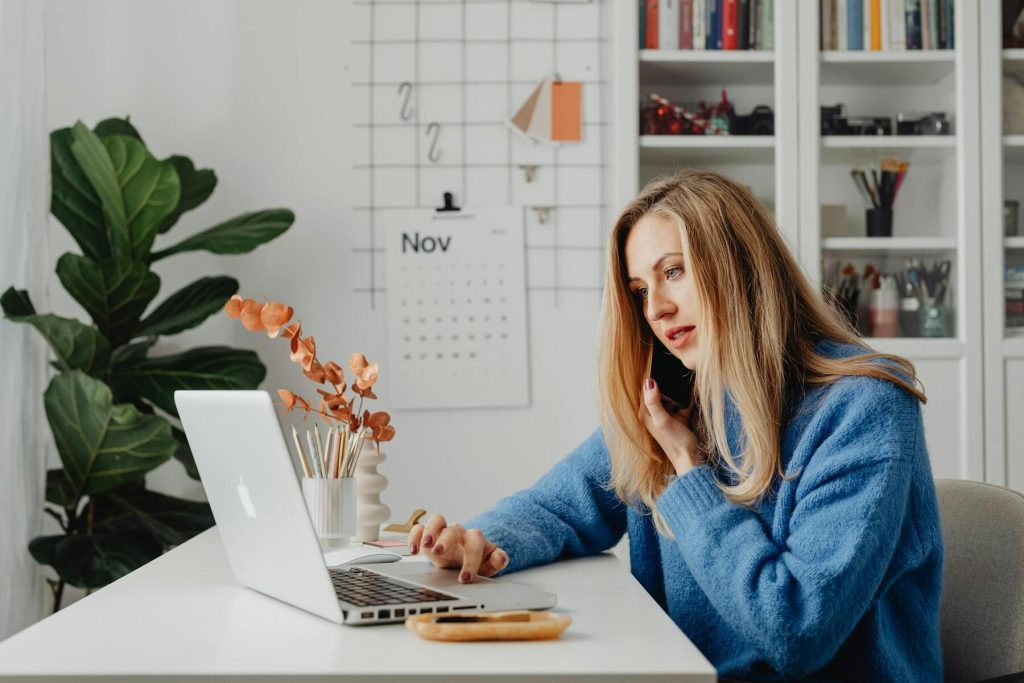 A woman sitting at a desk, using a laptop, with a phone nearby