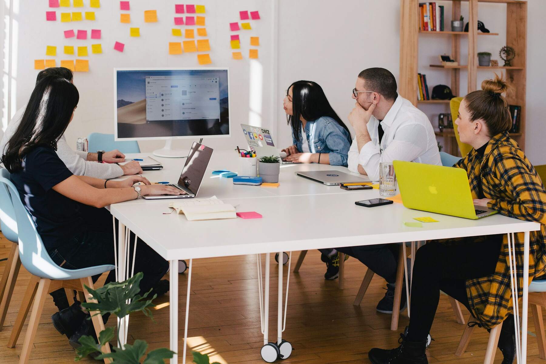 A diverse group of people seated around a table, each using laptops, engaged in discussion and collaboration