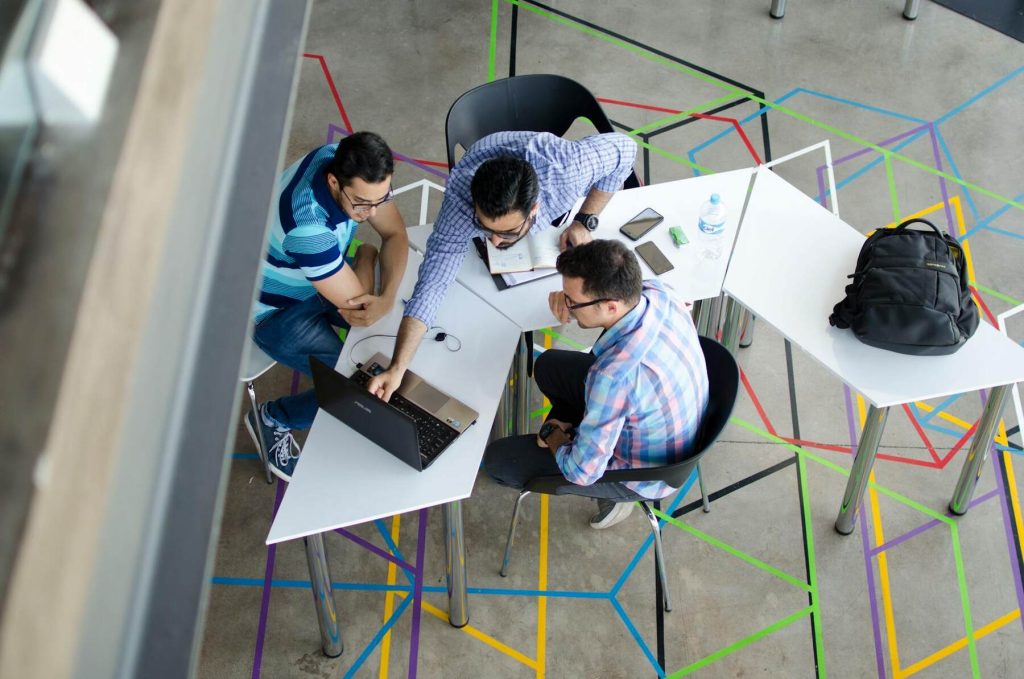 Three people around a table, each with a laptop, collaborating on a project in a modern office setting