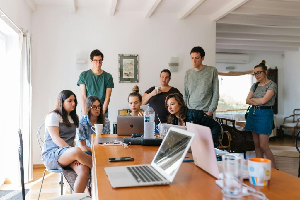 A diverse group of individuals seated at a table, each using laptops, engaged in discussion and collaboration