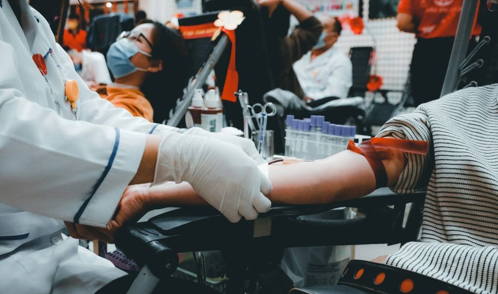 A blood donation scene showing a donor in a chair and a medical staff member taking blood