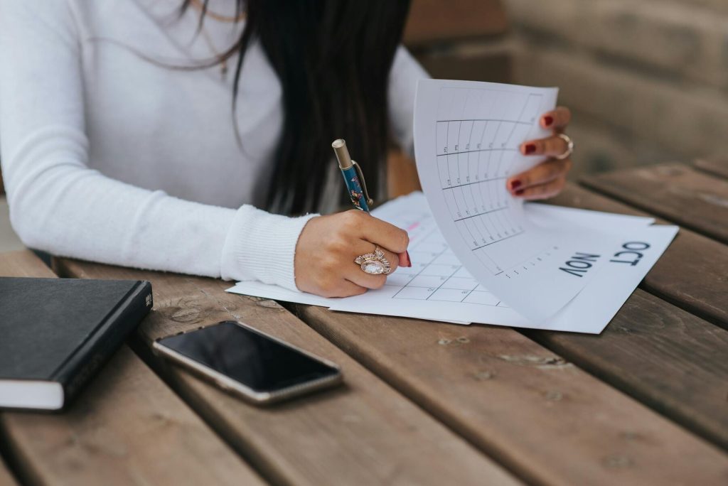 A woman writing on a calendar while holding papers and a pen